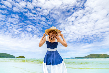 Happy Woman in summer vacation wearing hat and dress enjoying the view at the island beach.