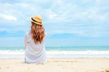 Happy Woman in summer vacation wearing hat and sitting, enjoying the view at the island beach.