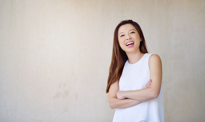Laughing young Asian woman standing by a wall outside