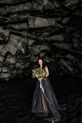 bride in black clothes stands in a black cave on a black sand beach near the Atlantic Ocean in Iceland