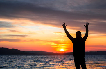 Fototapeta premium silhouette of a happy unrecognizable man at sunset on the lake