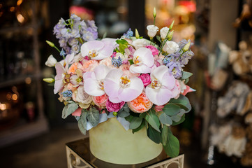 Green round box full of different tender color roses, orchids and bellflower decorated with green leaves
