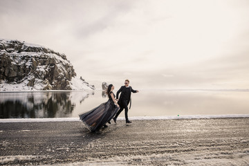 Young beautiful wedding couple in black clothes stands on the road against the backdrop of...