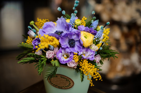 Green box of purple tender color flowers and yellow mimosa decorated with green leaves