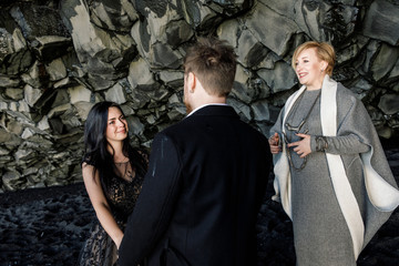 wedding ceremony in a black cave on a black sand beach in Iceland near the Atlantic Ocean. Bride in black dress groom in black clothes