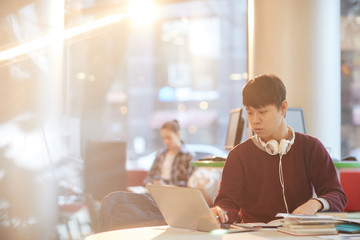 Obraz premium Asian college student using laptop computer while sitting at the table in the library