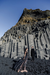 Young beautiful couple bride and groom in black clothes walks near basalt stones in Iceland