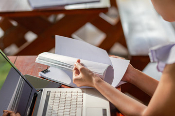 woman opening and reading a paper sheet near laptop on wooden table.