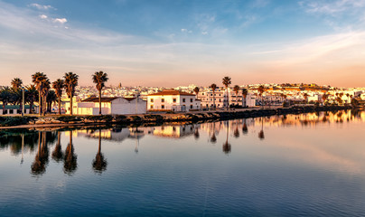 Panoramic view of the beach town of Conil de la Frontera, Spain, at dusk, and reflections on the calm waters of Salado river.