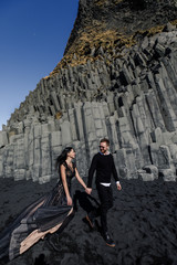 Young beautiful couple bride and groom in black clothes walks near basalt stones in Iceland