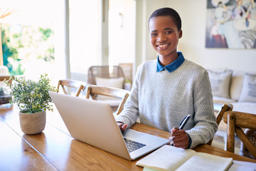 Smiling African American female entrepreneur sitting at home working online