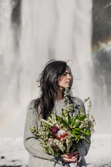 young beautiful wedding bride in black clothes stands near a waterfall in Iceland