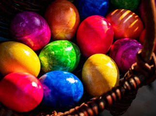 Fototapeta na wymiar Close-up of Easter eggs in various colors collected in wicker basket on sunny April morning (springtime). Egg hunt German Easter season holiday tradition. Horizontal format