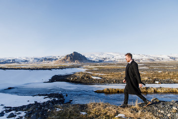 male traveler in black clothes is walking on the road against the background of mountains in Iceland