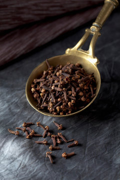 Brass spoon with whole cloves on textile, close up