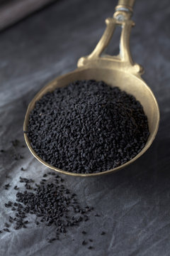 Brass spoon with black cumin on textile, close up