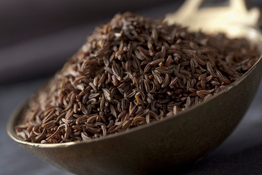 Brass spoon with caraway on textile, close up