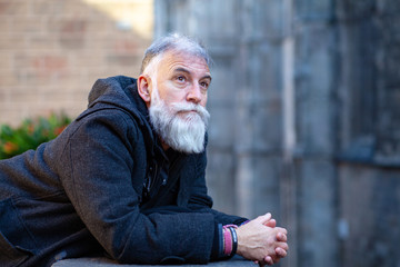 older man with white beard with thoughtful face looking up leaning on a street balcony