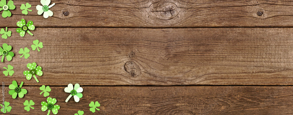 Poster St Patricks Day banner with corner border of handmade paper button shamrocks. Top view over a rustic wood background with copy space.