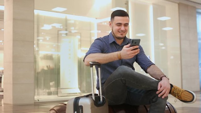 Young men on business trip uses mobile Internet at the airport. Laughs and writes a message in love