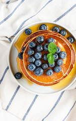 Pancakes with honey and blueberries in a plate on a light background, top view. Sweet tasty breakfast, dessert. American pancakes with berries.
