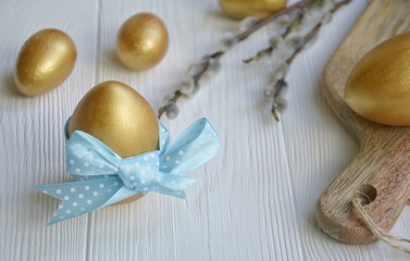 Fototapeta na wymiar gold easter eggs with decorative blue bow with willow branches on a light background with space for text