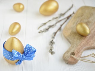 gold easter eggs with decorative blue bow with willow branches on a light background with space for text