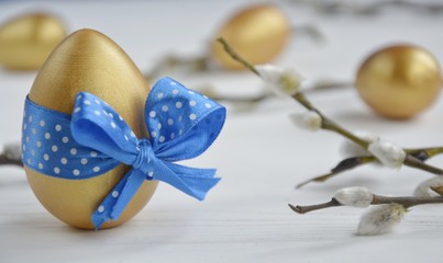 Fototapeta na wymiar gold easter eggs with decorative blue bow with willow branches on a light background with space for text