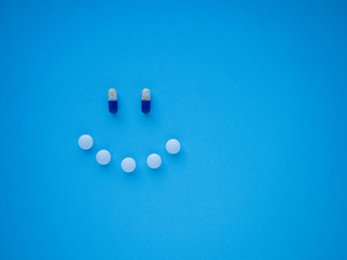 Happy smiley face made of blue and white tablets and pills on blue background top view with copy...