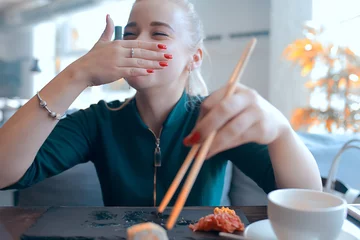 Gordijnen girl eats sushi and rolls in a restaurant / oriental cuisine, Japanese food, young model in a restaurant © kichigin19