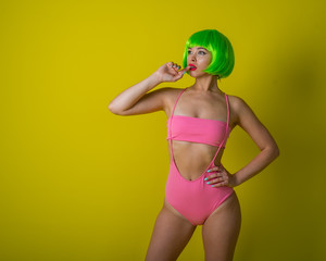 Beautiful woman in a green short wig and pink bikini posing on a yellow background. Portrait of a girl with sensual red lips.