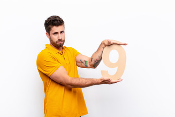 young handsome man sad, depressed, unhappy, holding a number 9.