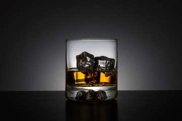 Whiskey with ice in a glass individually on a black background with a slight white light from behind