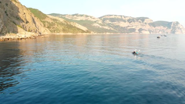 Aerial view of a kayak in the middle of the sea. Drone flight above two people kayakers paddling at sunset. Colorful sport kayak silhouette. Beautiful sea landscape at summer sunset.