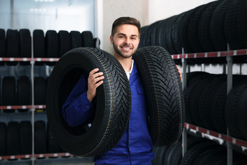 Male mechanic with car tires in auto store - obrazy, fototapety, plakaty