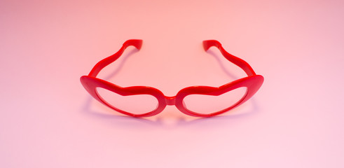 Red glasses in the shape of hearts on a pink background.