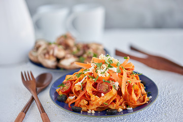  Front view of pasta with tomato, carrots, grated egg and parsley, and another dish of sauteed sittake mushrooms with bacon and parsley on a white background.