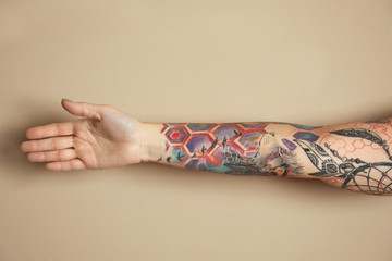 Woman with colorful tattoos on arm against beige background, closeup