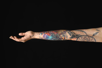 Woman with colorful tattoos on arm against black background, closeup