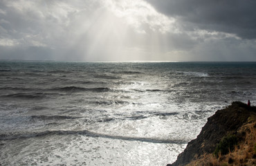 Unrecognized person standing the edge of a cliff end enjoying the dramatic stormy sea.