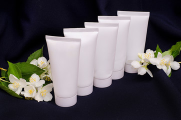 White tubes for creams on a background of spring white flowers of an apple tree on a black and blue background. For advertising cosmetics. Gift