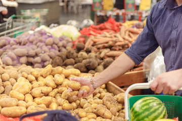 Man takes potatoes at a vegetable market or grocery store. Purchases of vegetables, close-up
