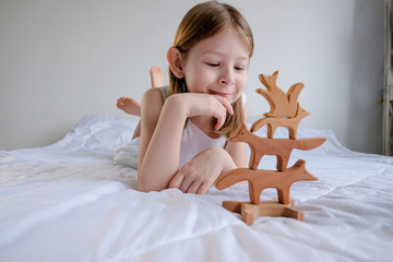 little girl of 8 years old plays with eco-friendly wooden toys in the shape of different animals