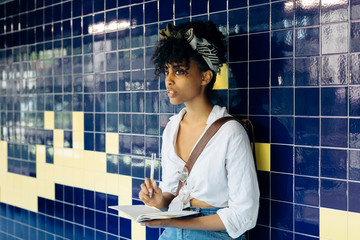 Portraitof young woman with notebook leaning against tiled wall looking at distance