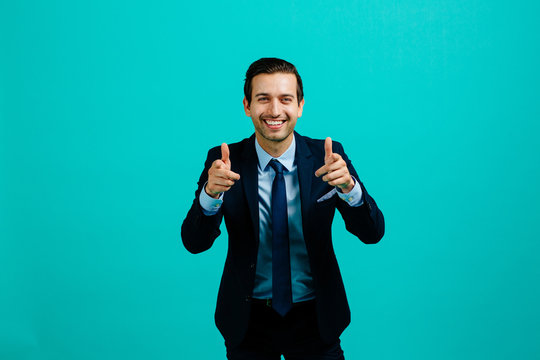 Portrait of a young entrepreneur business man smiling, pointing at camera with index finger, positive attitude. isolated on blue studio background