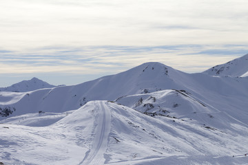 Fototapeta na wymiar High winter mountains with ski trace, road in snowy slopes