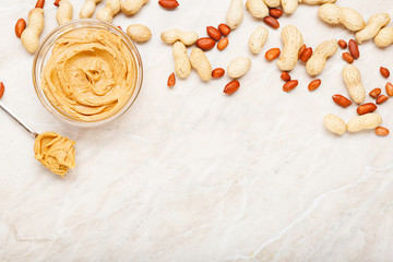 Fototapeta na wymiar Peanut butter in glass plate with peanuts in shell, peeled peanuts, spoon with peanut butter. Creamy peanut paste flat lay with place for text on white marble background for cooking breakfast.