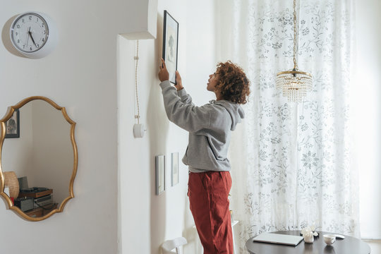 Young woman hanging up picture at home