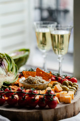 Delicious gourmet food degustation in Paris, France. Artichoke creme mousse, cheese, ripe red tomato, olives, corn chips. Two glasses of expensive white wine. Rusic wooden board, close up, front view