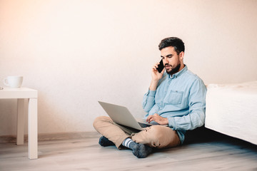 Man talking on smart phone while using laptop computer sitting at home